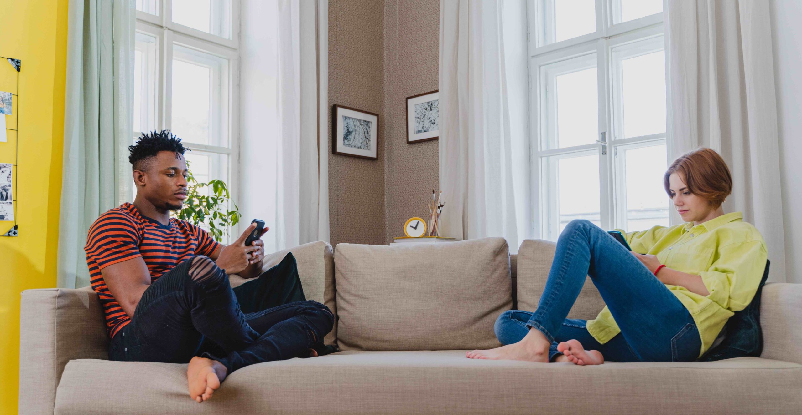 oung mixed couple addicted to smartphones sitting on sofa at home.